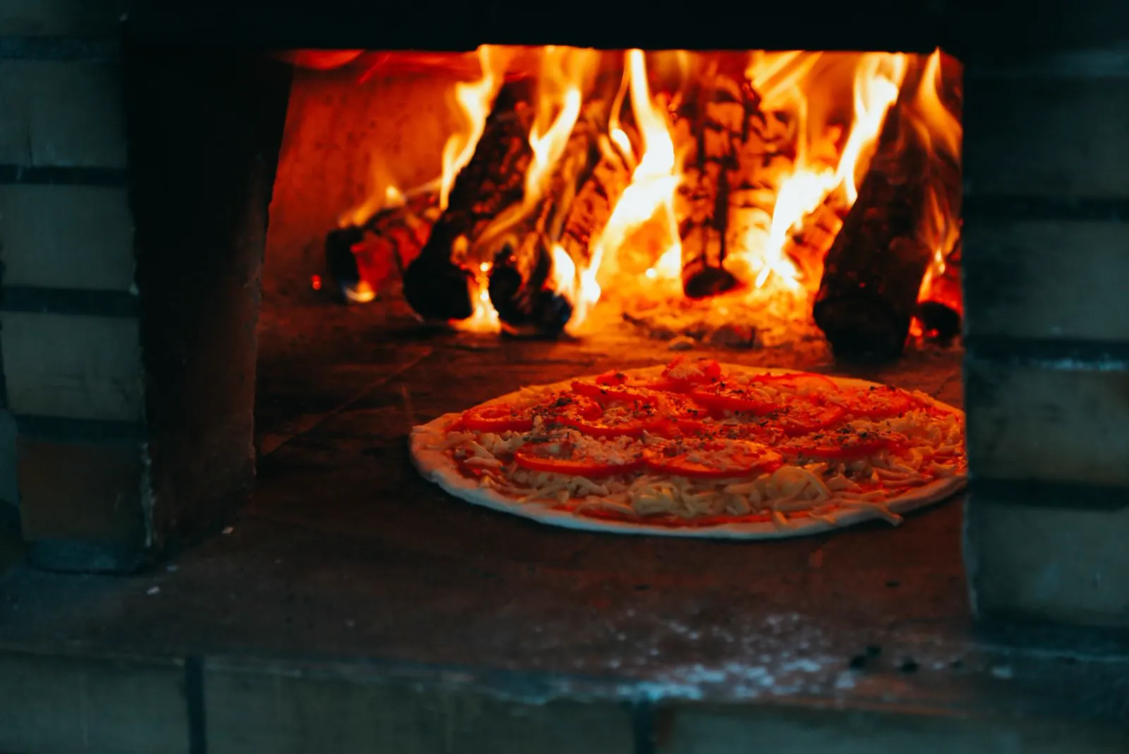 Pizza backt im Holzofen, dahinter brennt das Holz