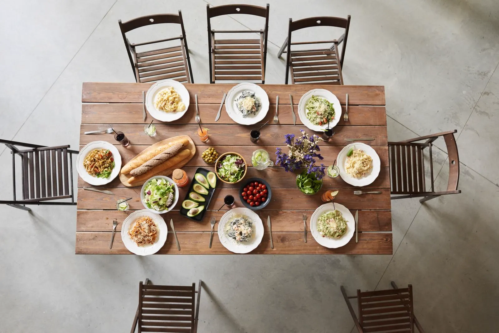 Gedeckter Holztisch von oben mit Pastatellern, Brot, Salat und Gläsern
