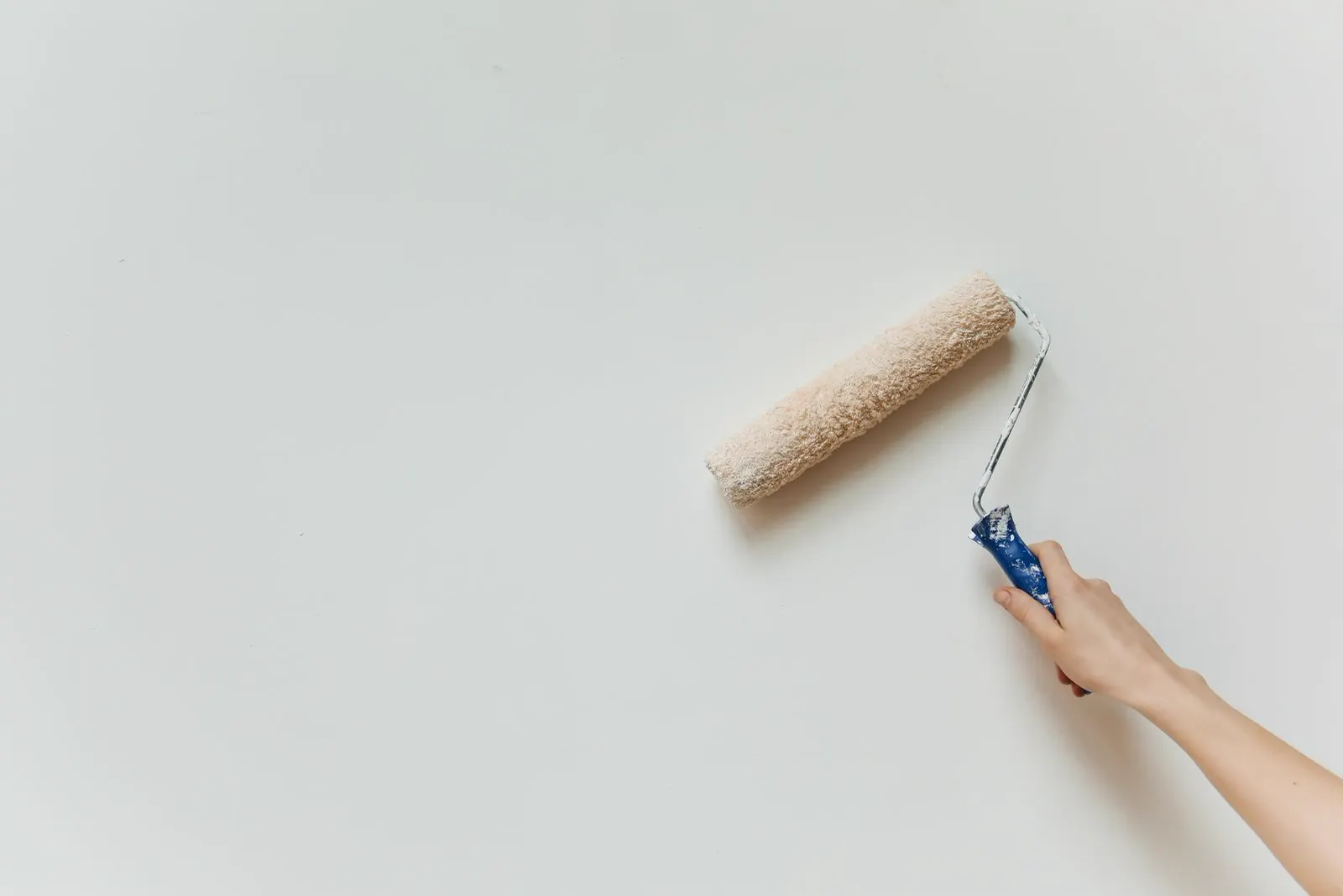 Hand führt eine Farbrolle über eine weiße Wand