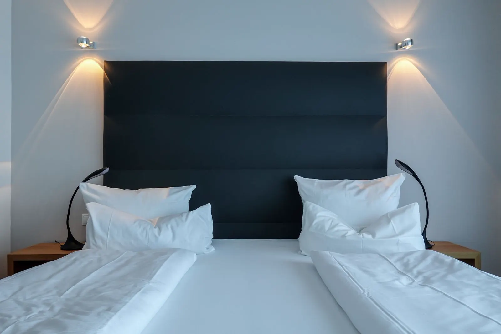 Bett mit weißer Bettwäsche und dunklem Kopfteil, zwei Leselampen
