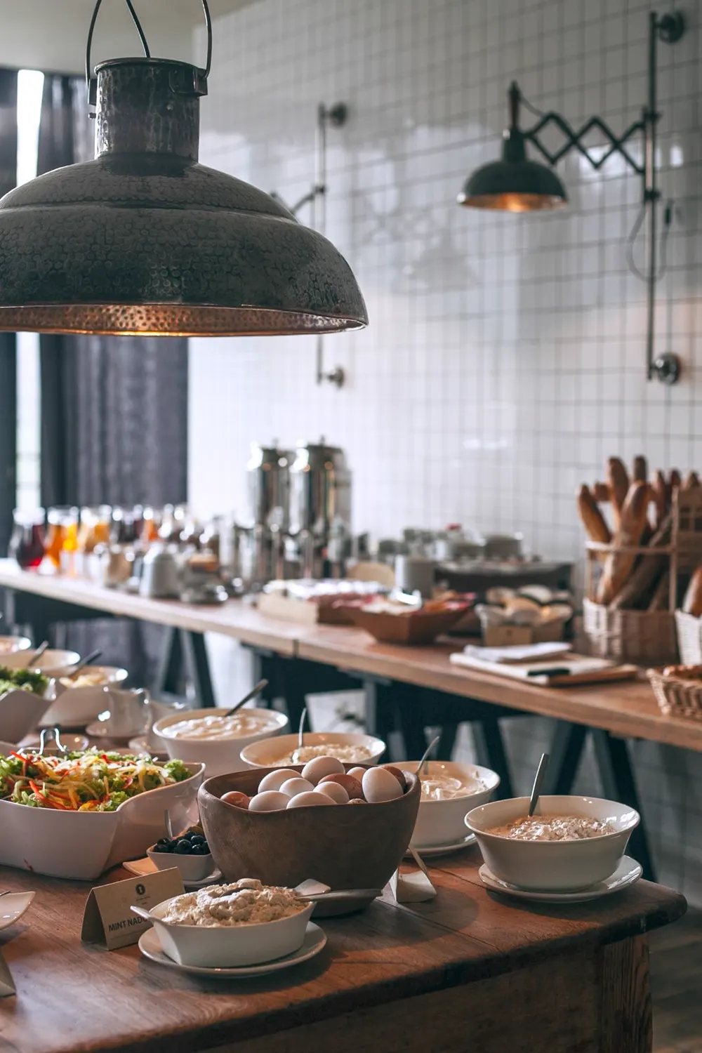 Frühstücksbuffet mit Salat, Eiern, Aufstrichen und Brot auf langen Holztischen