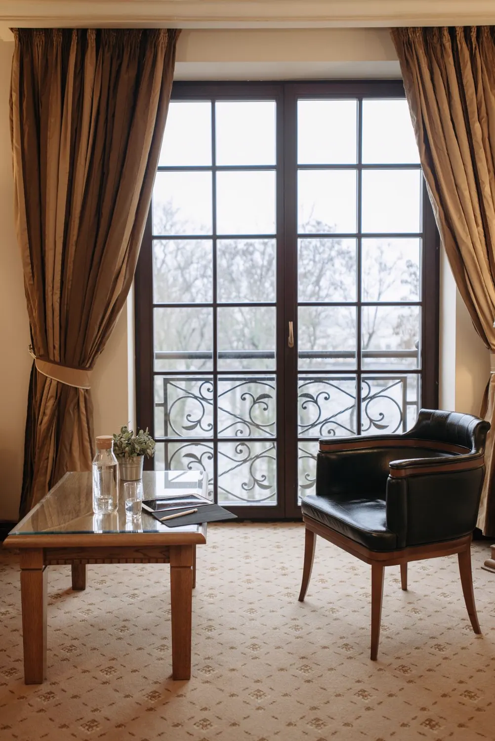 Sitzecke mit Tisch und Sessel vor einer bodentiefen Fenstertür mit Geländer